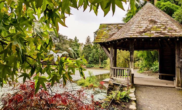 Late summer, early autumn colour surrounds the Boathouse alongside the Skating Pond at Bodnant Garden, Conwy, North Wales